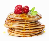 Small pancakes topped with honey, raspberries and mint on white background