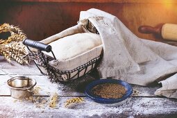 Dough in proofing basket on wooden table with flour, cumin and wheat ears