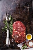 Rohes Ribeye Steak mit Gewürzen und Fleischgabel auf dunklem Hintergrund