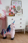 Unicorn pinata in front of chest of drawers decorated with number 5 made from paper flowers