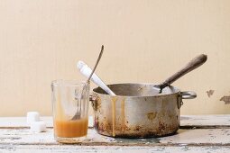 Alter Aluminium-Topf und hausgemachte Karamellsauce in Glas auf weißem Holztisch