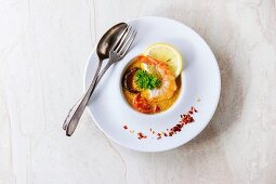 White plate with Spicy Thai soup Tom Yam with Coconut milk, Chili pepper and Shrimp over white marble as background