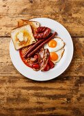 Englisches Frühstück mit Spiegeleiern, Würstchen, Speck, Bohnen, Toast, Tomaten und Pilzen