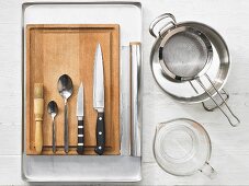 Various kitchen utensils: pot, sieve, baking tray, pastry brush, spoons, knives