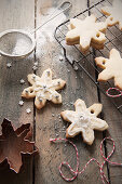 Homemade snowflake shaped Christmas tree decoration biscuits cooling on a wire rack and being iced and decorated in the backgroun is a mini sifter with icing sugar and a copper cookie cutter and bakers twine
