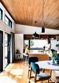 Offene Küche und Essbereich mit Parkettboden, Holzdecke und Terrassentür, im Hintergrund Mutter und Sohn