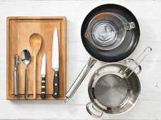 Various kitchen utensils: pan, measuring cup, pot, strainer, peeler, knives, spoon