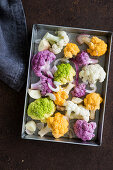 Colourful cauliflower florets with garlic and onions on a baking sheet