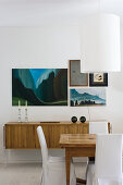 Pictures on wall above retro sideboard behind rustic dining table and loose-covered chairs