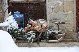 Snowy firewood and pine branches on old wooden sledge against stone façade