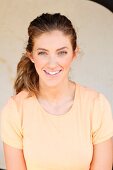 A young woman wearing an orange T-shirt in front of a light background