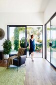 Black leather armchair in bright living area with patio doors, woman in the background