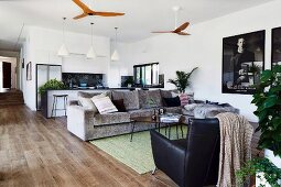 Open living area with black armchair, sofa set and ceiling fan, pendant lamp above kitchen island in background