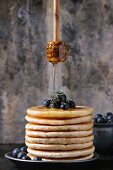 Pancakes with fresh blueberries in blue ceramic plate, and flowing honey from wooden honey dipper