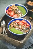 Green smoothie bowls with fresh strawberries, granola, chia and pumpkin seeds, dried fruit and nuts