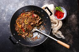 Stir-fry soba noodles with beef and vegetables in wok pan on dark background