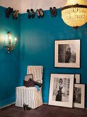 Large black and white photos, easy chair, sconce lamp and chandelier in cloakroom with shoes hung on picture rail on blue walls