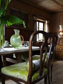 Antiker Stuhl mit grünem Polster am gedeckten Tisch in einer Bauernstube