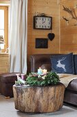 Advent wreath with four colourful candles on tree-stump coffee table in front of leather sofa
