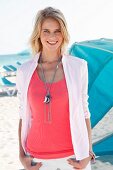 A blonde woman wearing a pink top, a white shirt and a necklace on the beach