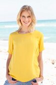 A blonde woman wearing a yellow T-shirt and jeans on the beach