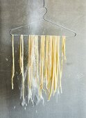 Homemade tagliatelle hanging on a wire coat hanger to dry