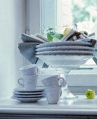 Plates stacked on cake stand and white coffee service on windowsill
