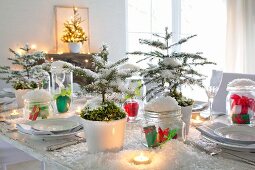 Christmas table decorated with artificial snow, small fir trees, white crockery and lit tealights