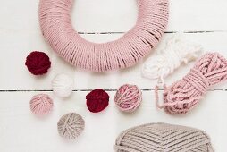 Balls of wool and wreath wrapped in pink yarn on white surface