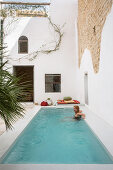 Woman relaxing in swimming pool in front of partially rendered stone wall