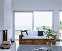 Wicker couch with white seat cushions and scatter cushions in front of sliding terrace doors with sea view