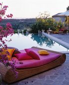 Rattan lounger with hot-pink cushions and scatter cushions in front of swimming pool