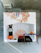 Colourful textiles and stacked pouffes in white cube in front of concrete wall