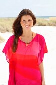 A brunette woman wearing a pink tunic on the beach