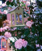 Tealight holders shaped like birdhouses amongst flowering roses