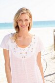 A blonde woman wearing a white embroidered T-shirt on the beach