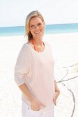 A blonde woman wearing an orange top and white long-sleeved top on the beach