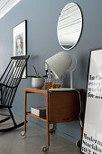 Retro wooden trolley below round mirror on grey wall