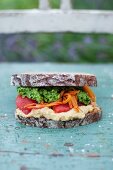 Vegan sandwich made from rye bread with corn hummus, roasted red pepper, carrot and parsley pesto