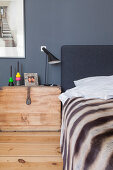 Wooden trunk used as bedside table next to bed against grey wall
