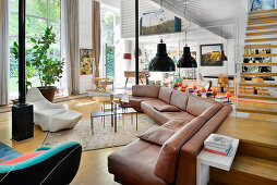 Brown leather corner sofa and designer armchairs in open-plan interior