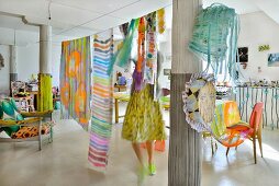 Woman hanging fabrics from line in loft apartment with columns and colourful eclectic furnishings