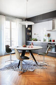 Round dining table and retro chairs on zebra-skin rug in grey fitted kitchen