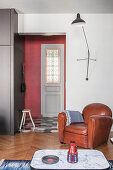 Leather armchair under wall-mounted lamp next to open doorway leading into hall