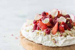 Rose and pistachio pavlova with fresh strawberries and raspberries, decorated with pistachio nuts and dried and fresh rose petals on a white and grey marble surface