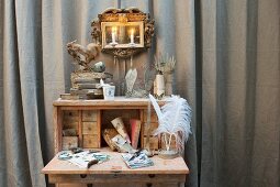 Various vintage accessories on writing desk and gilt-framed mirror sconce in front of grey curtain