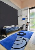 Narrow bed against fitted cupboards with many different compartments and colourful rug in foreground