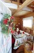 View of set table in wooden cabin seen through open wooden door with wreath