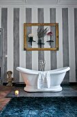 White, free-standing bathtub below gilt picture frame and ornaments on grey-striped wall