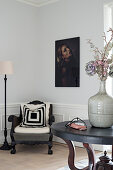 Dried flowers in stoneware vase on round table in front of antique armchair